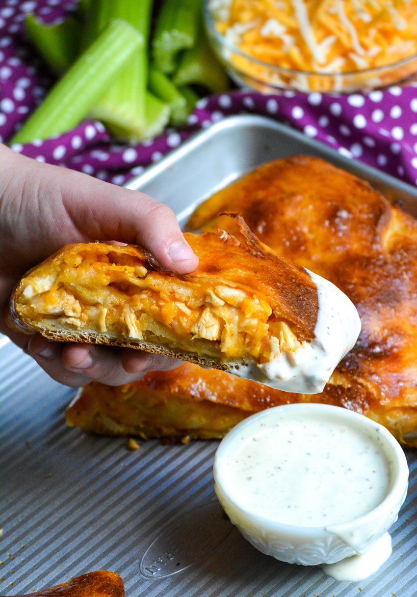 a hand holding a piece of buffalo chicken stuffed stromboli and dipping it into a small white bowl filled with ranch dressing