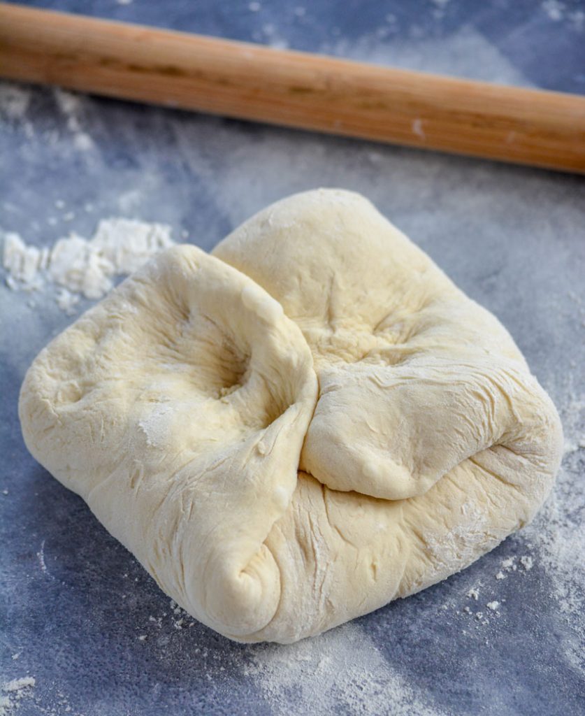 Grandma's homemade pizza dough recipe has been punched down and folded on a gray background with a wooden rolling pin