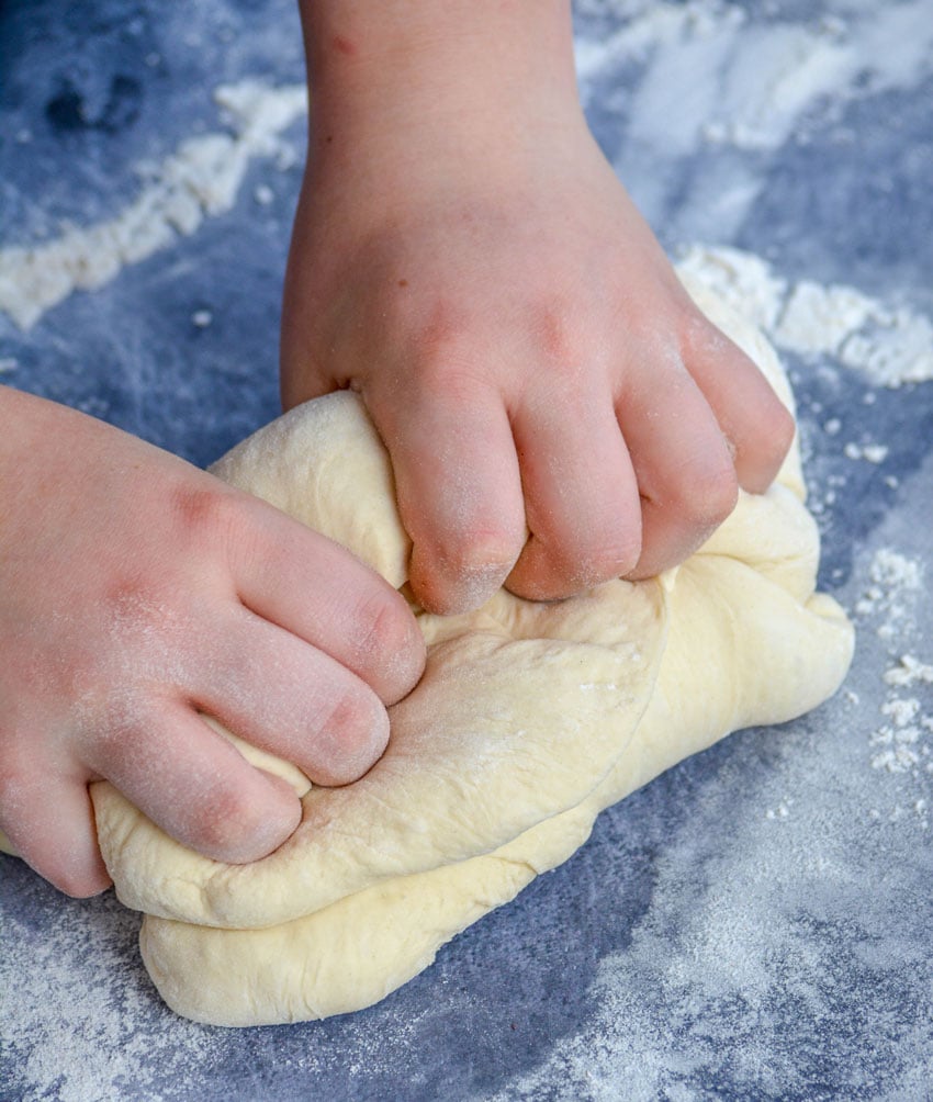 kid friendly pizza dough recipe being kneaded by little hands on a floured gray surface