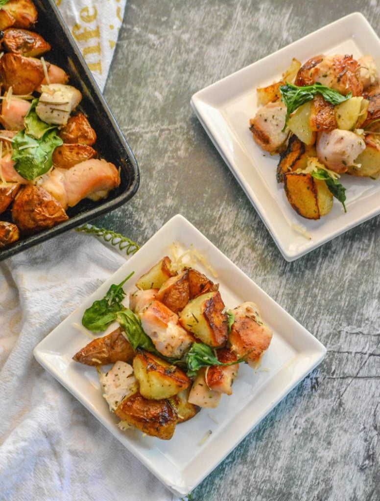 two white plates topped with roasted chicken, potatoes, and spinach on a dull background