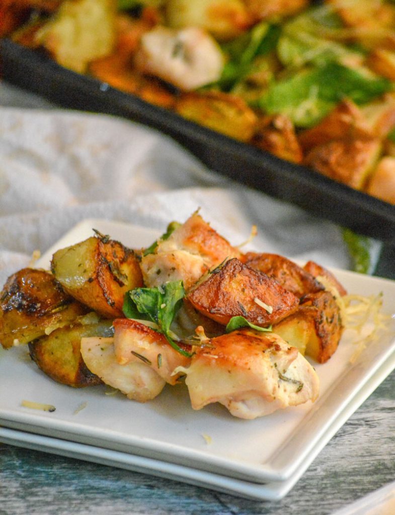 Roasted Chicken and Vegetable Sheet Pan Supper on a stack of two white plates with the sheet pan pictured in the background