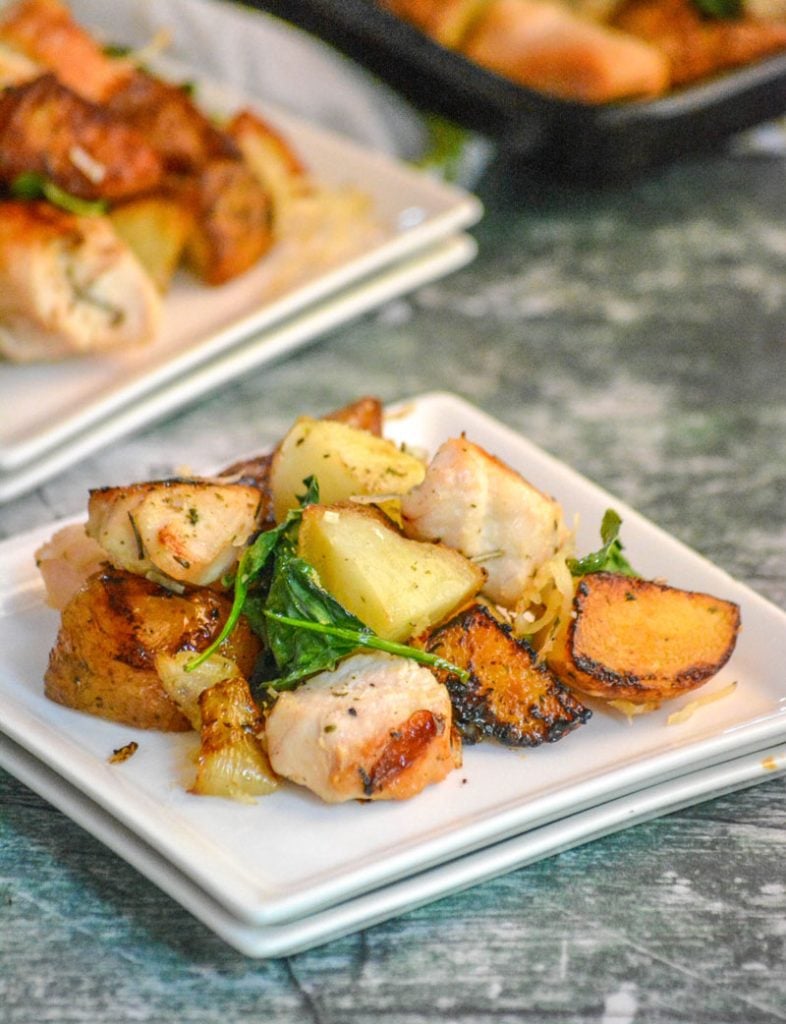 roasted chunks of chicken and potatoes with crispy spinach leaves on white plates