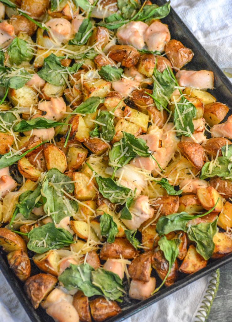 Roasted Chicken and Vegetable Sheet Pan Supper shows spinach, chopped chicken, and roasted potatoes cooked on a single pan and topped with shredded Parmesan cheese