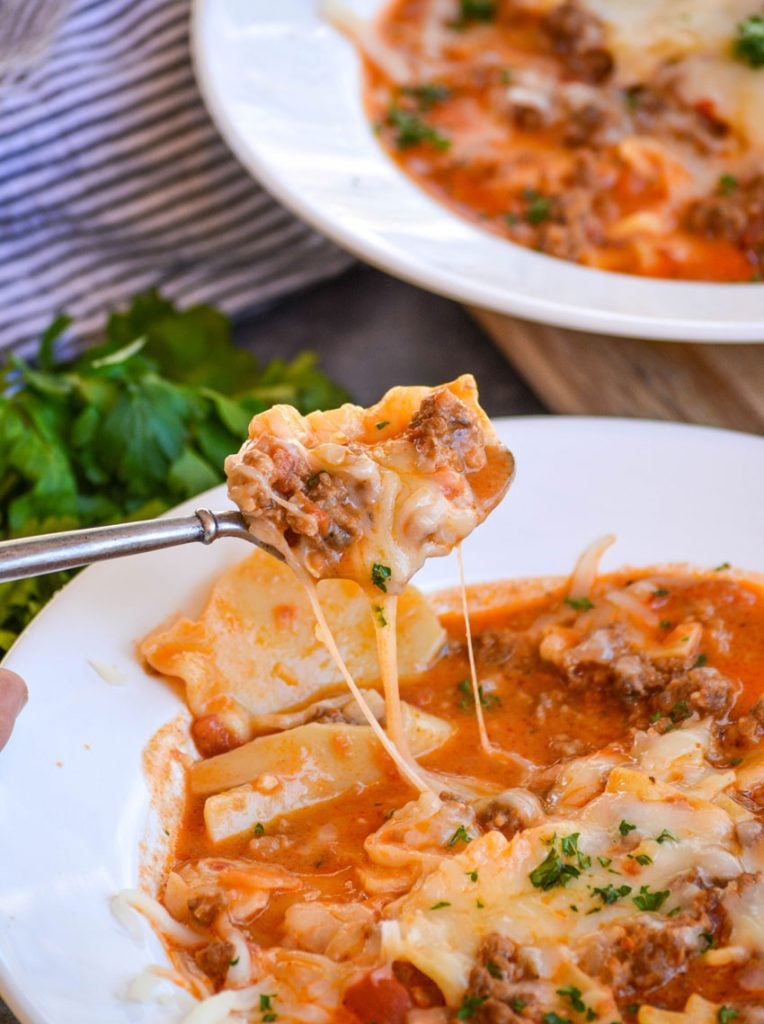 a spoonful of lasagna soup held up with mozzarella cheese pull from the bowl