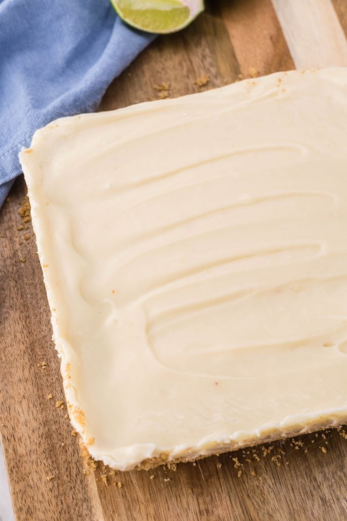 a slab of key lime pie fudge shown on a wooden cutting board with fresh sliced lime wedges in the background