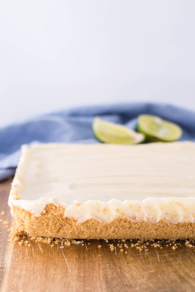 a slab of key lime pie fudge shown on a wooden cutting board with sliced limes in the background