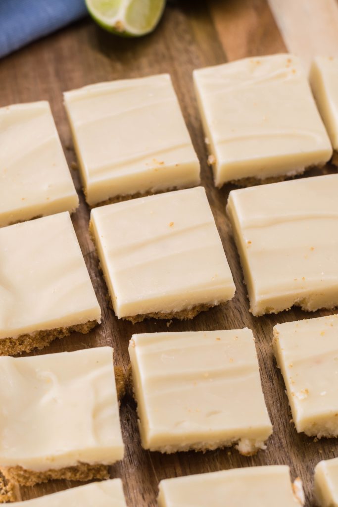 a slab of key lime pie fudge shown on a wooden cutting board with fresh sliced lime wedges in the background