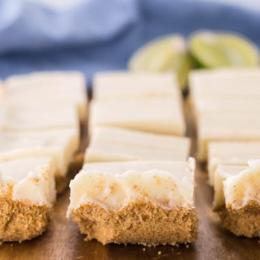 a slab of key lime pie fudge shown on a wooden cutting board with fresh sliced lime wedges in the background