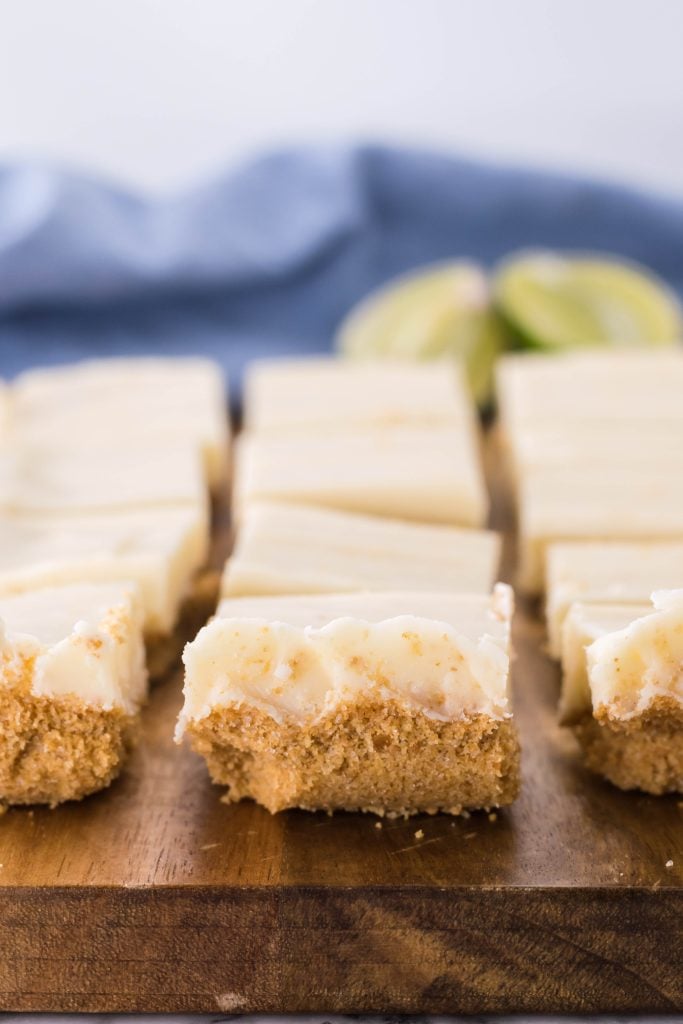 a slab of key lime pie fudge shown on a wooden cutting board with fresh sliced lime wedges in the background