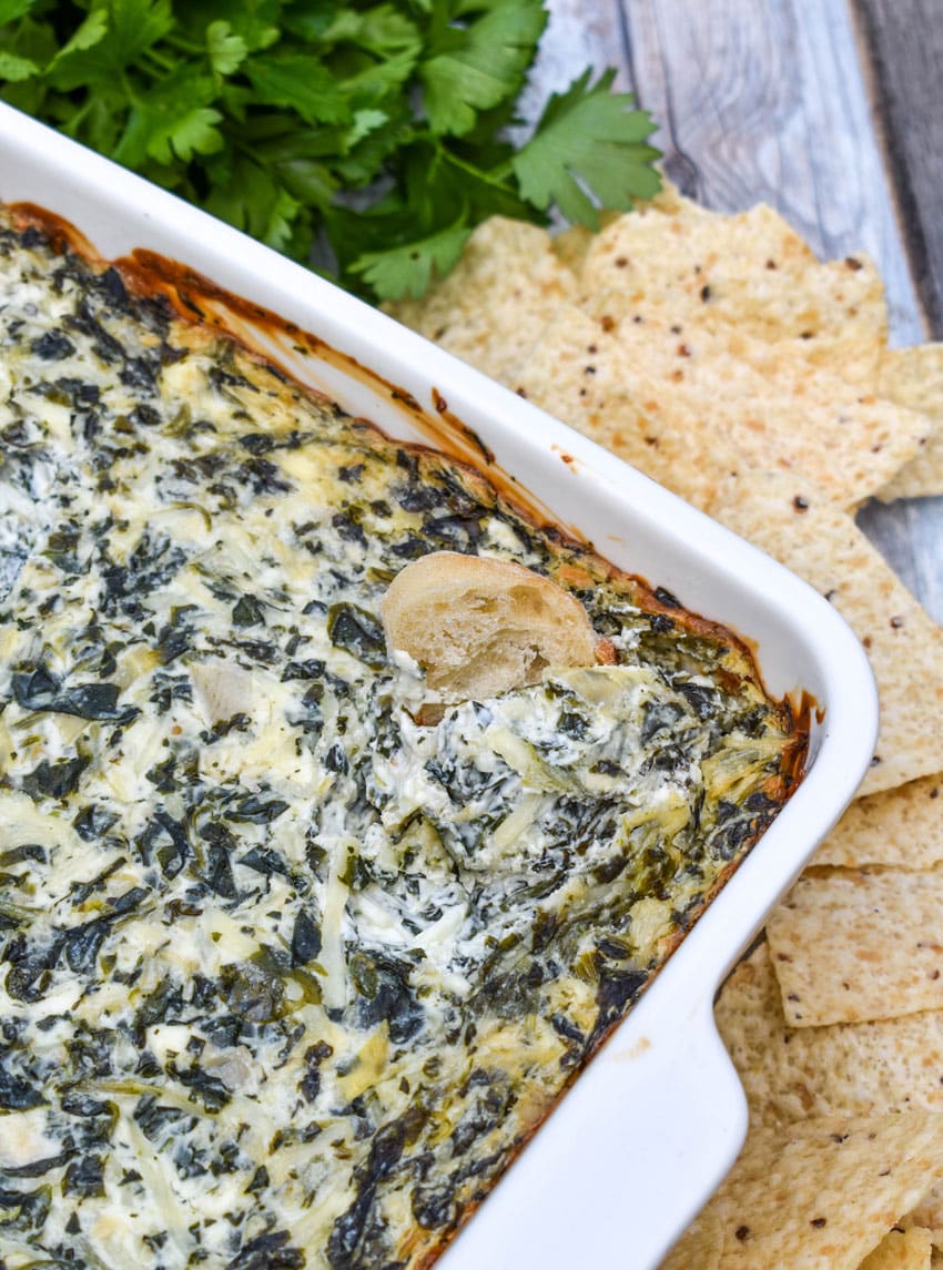 a slice of baguette bread in a baking dish filled with homemade spinach and artichoke dip