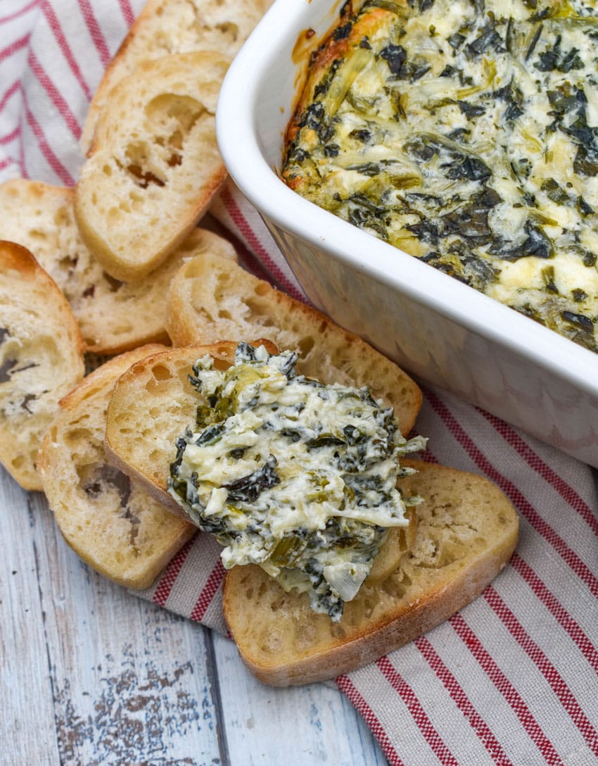 creamy spinach and artichoke dip on a slice of toasted baguette bread resting on a wooden table