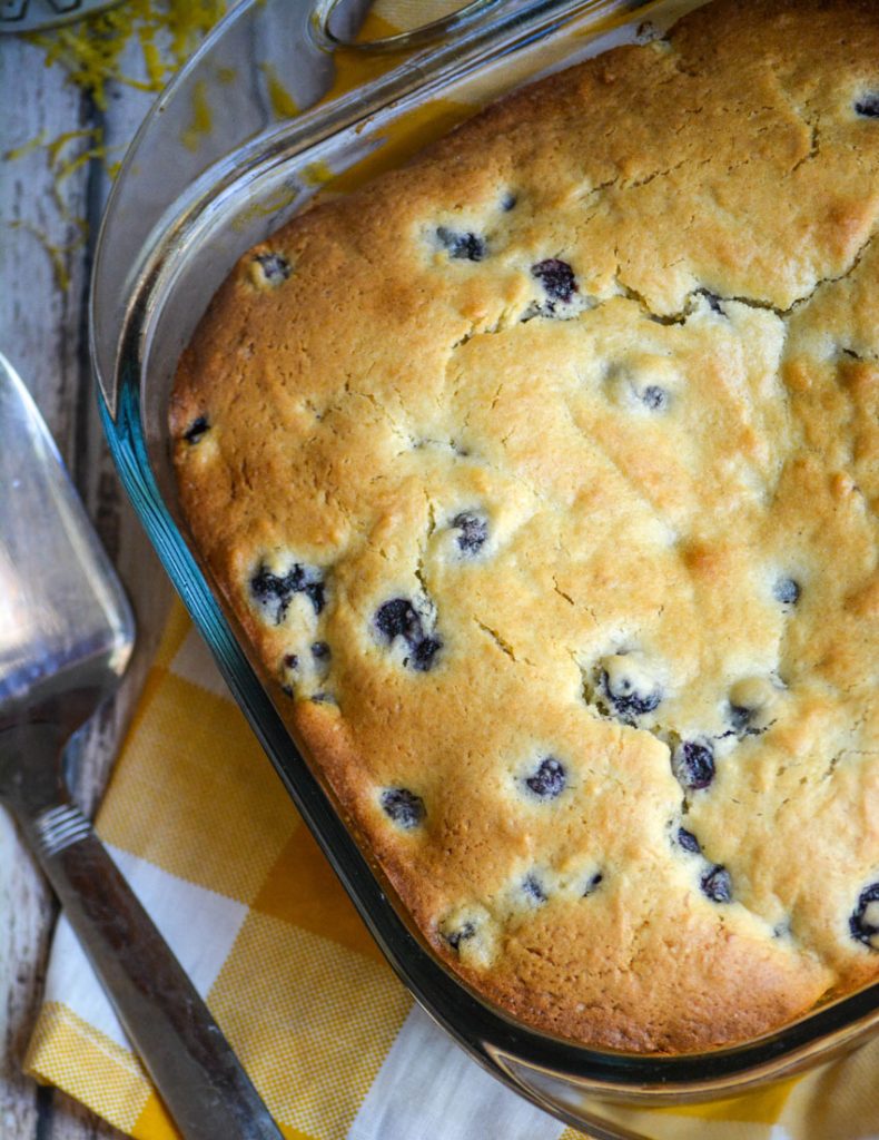 buttermilk blueberry breakfast cake on a wooden picnic table with yellow checkered napkin and metal spatula