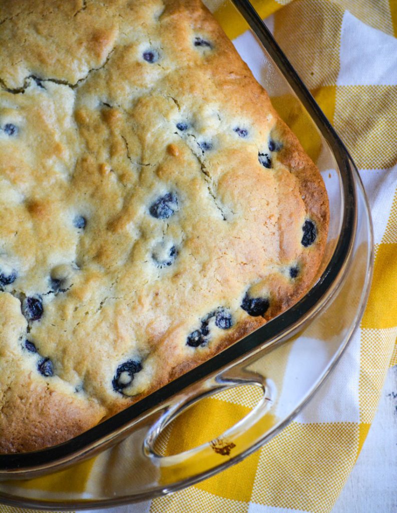 blueberry breakfast cake in a square glass dish on a white and yellow checkered cloth napkin