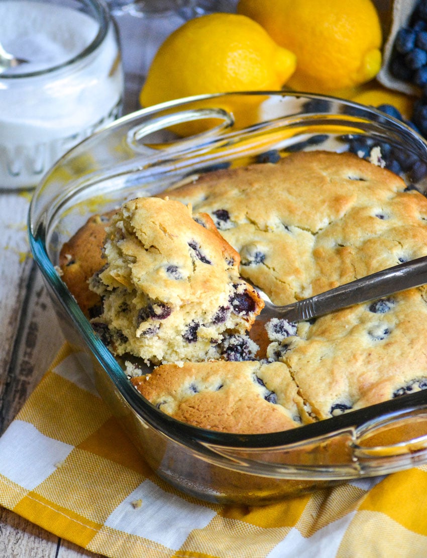 a spatula stuck in a buttermilk blueberry cake in a glass baking dish