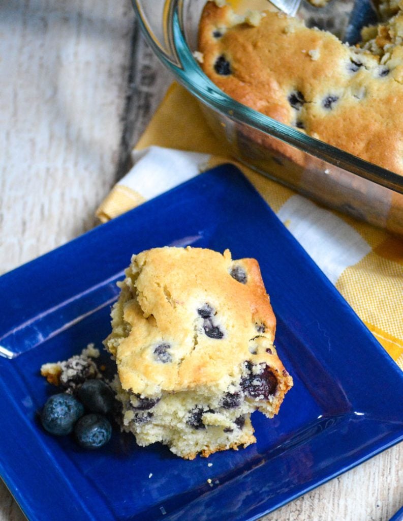 a slice of blueberry breakfast cake on a small blue square plate with fresh blueberries