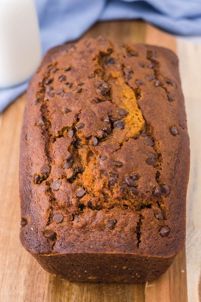 a loaf of crockpot pumpkin bread sliced open and shown on a cutting boar with fresh milk in the background
