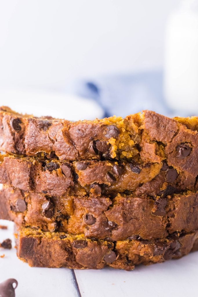 slices of crockpot pumpkin bread shown stacked with a glass of milk and scattered chocolate chips in the background