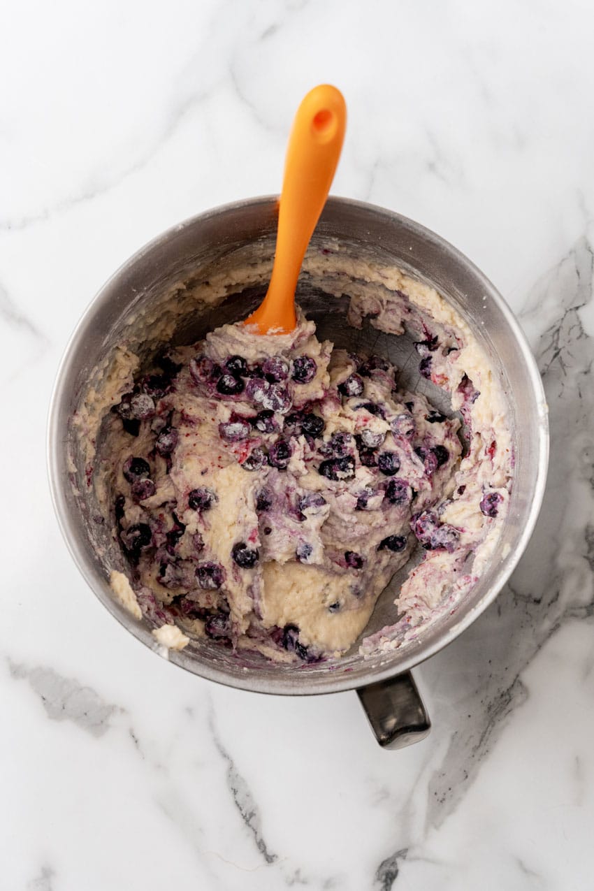 blueberries mixed into cake batter in a metal mixing bowl
