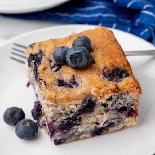a square of buttermilk blueberry breakfast cake on a small white plate with a silver fork on the side