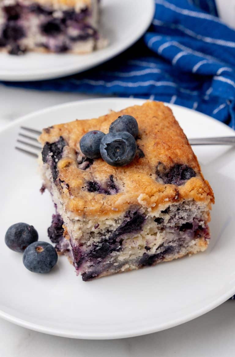 a square of buttermilk blueberry breakfast cake on a small white plate with a silver fork on the side