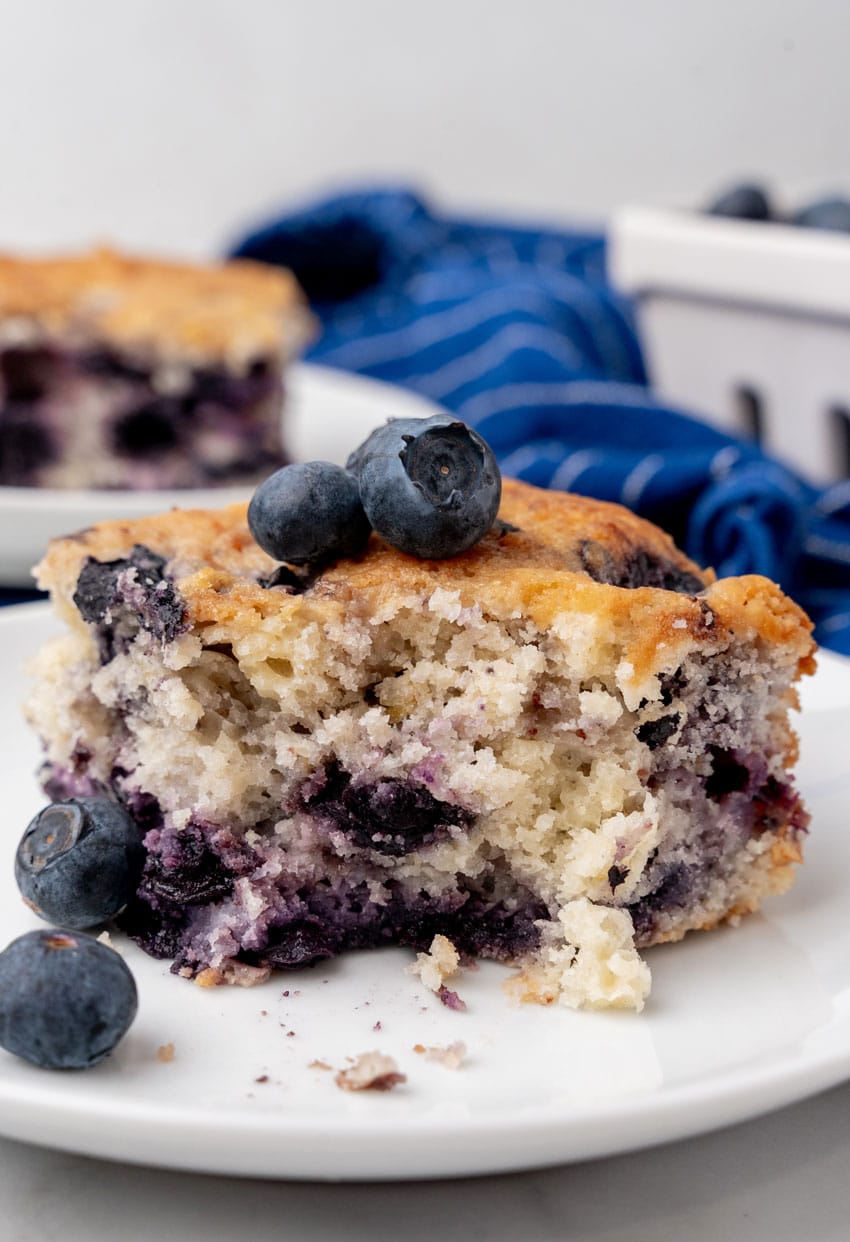 a slice of buttermilk blueberry breakfast cake on a small white plate with a silver fork on the side