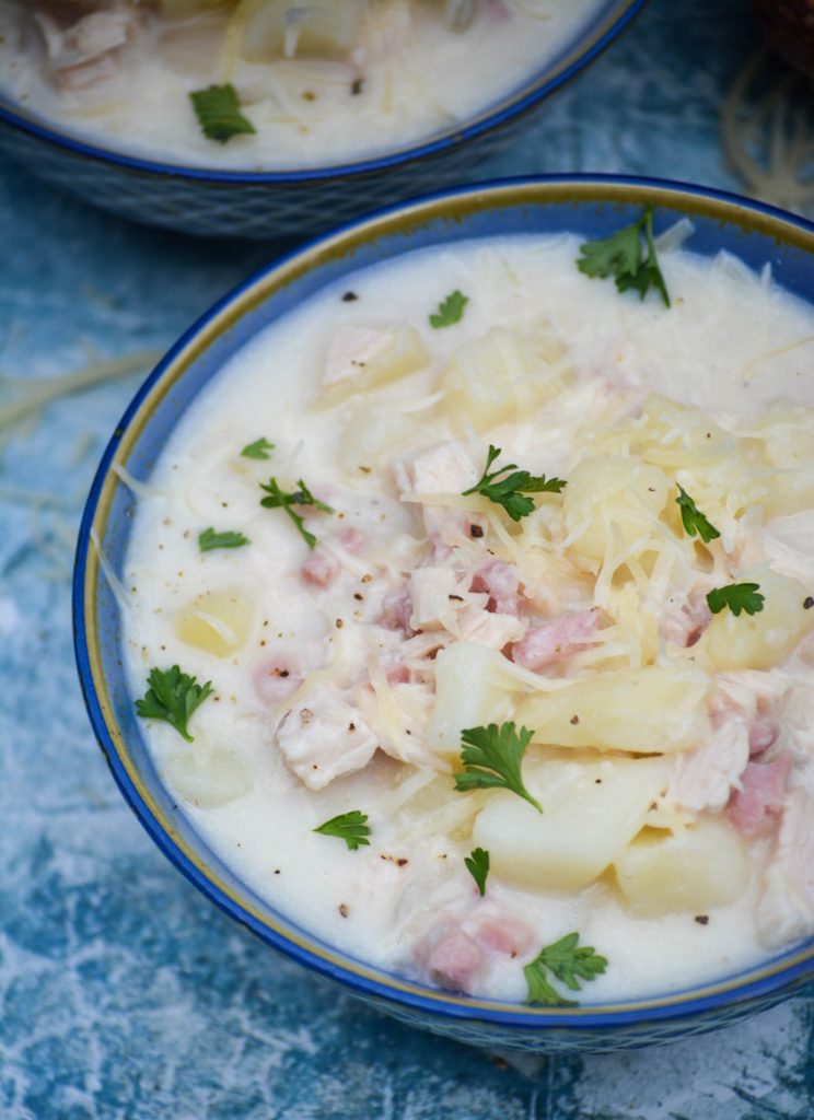 a bowl of chicken cordon bleu soup topped with shredded cheese and parsley on a blue background