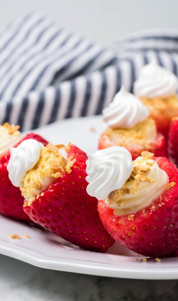 cheesecake stuffed strawberries on a white plate with a striped dish cloth in the background