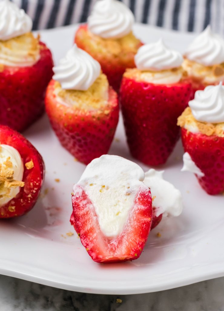 cheesecake stuffed strawberries on a white plate with one cut in half to show the filled inside