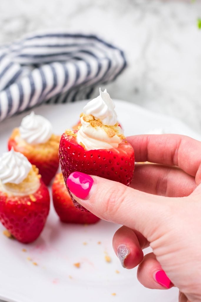 cheesecake stuffed strawberry being held up for a close up shot by a hand with pink nails