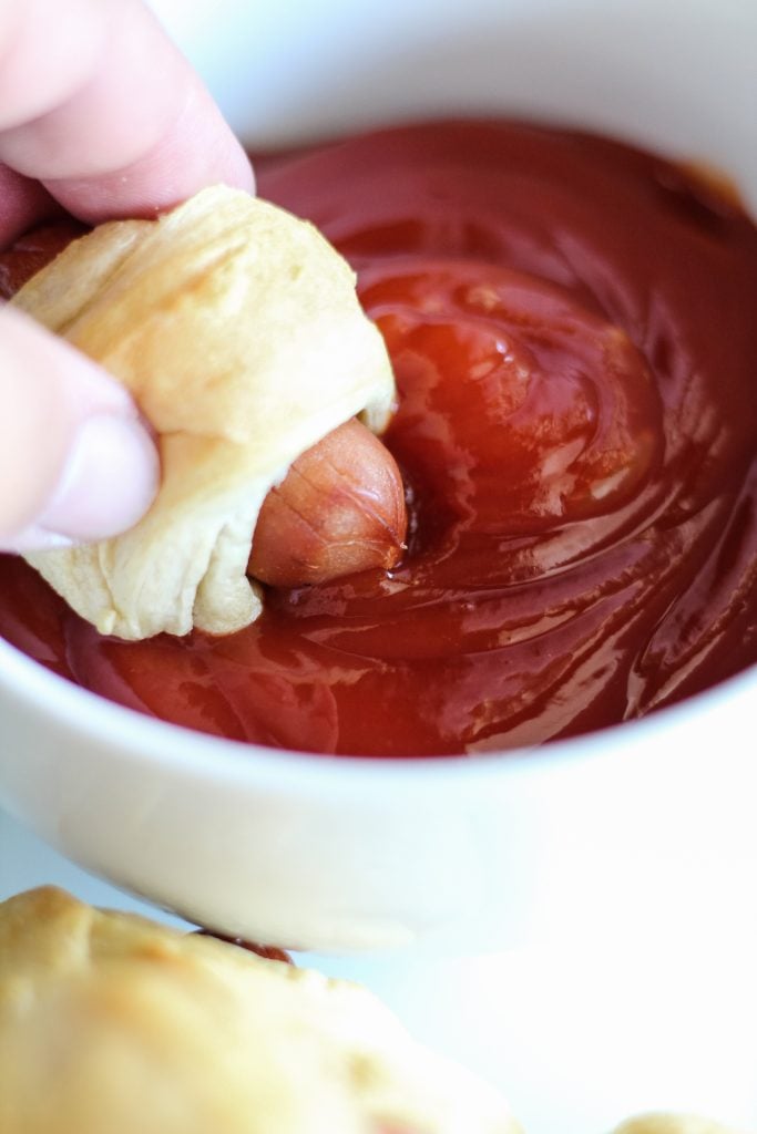 classic pigs in a blanket piled high on a white rectangular serving platter with a bowl of ketchup for dipping