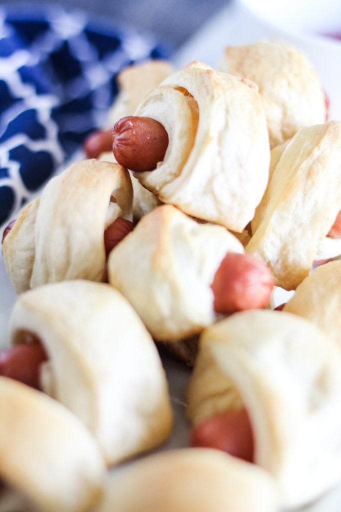 classic pigs in a blanket piled high on a white rectangular serving platter with a bowl of ketchup for dipping