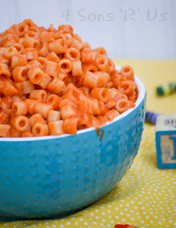 Homemade Spaghetti O's in a white rimmed blue bowl on a yellow background with crayons and wooden toy blocks