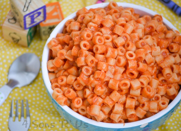 Homemade Spaghetti O's in a white rimmed blue bowl on a yellow background with crayons and wooden toy blocks