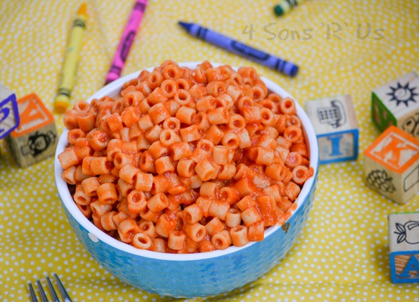 Homemade Spaghetti O's in a white rimmed blue bowl on a yellow background with crayons and wooden toy blocks