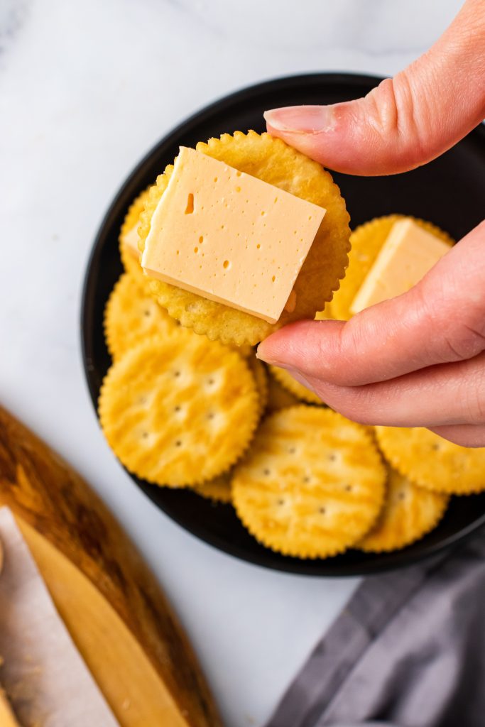a hand holding up a round cracker topped with a square of homemade velveeta style american cheese