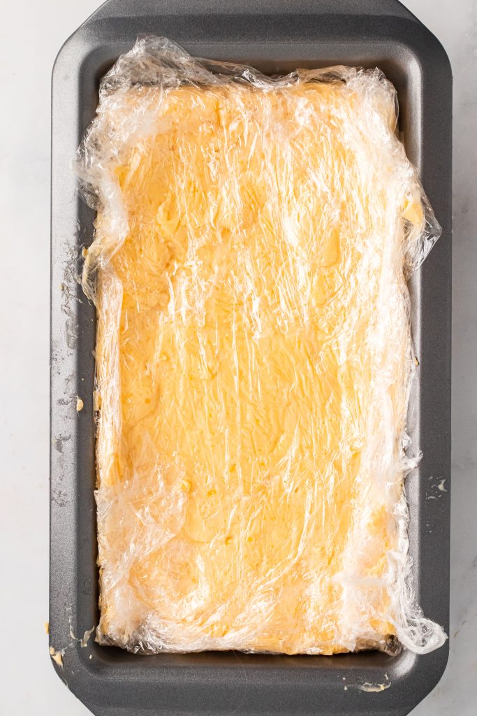 loaf of velveeta style american cheese wrapped in plastic wrap set in a metal loaf pan