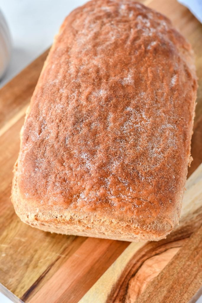 a loaf of honey wheat sandwich bread on a wooden cutting board