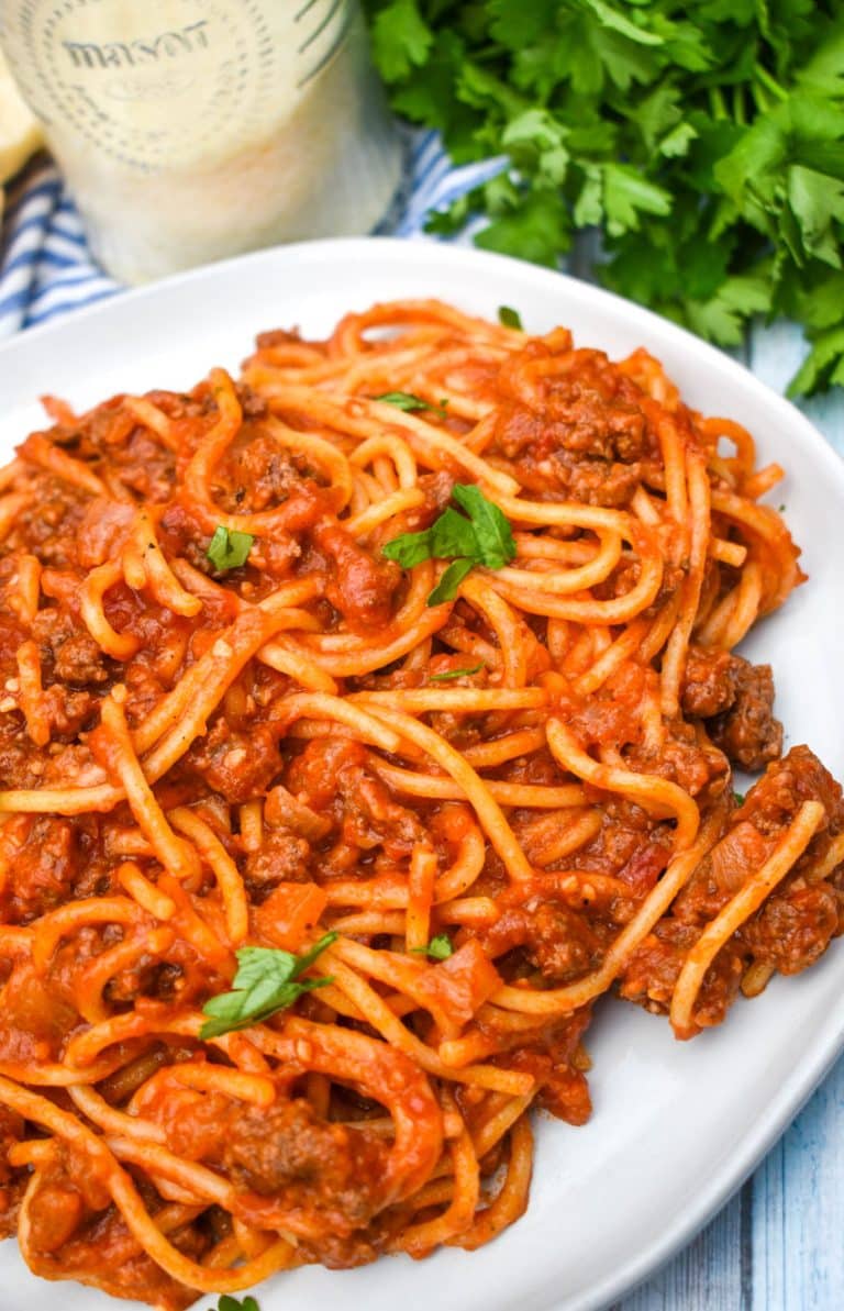 one pot spaghetti on a white plate with fresh herbs in the back ground