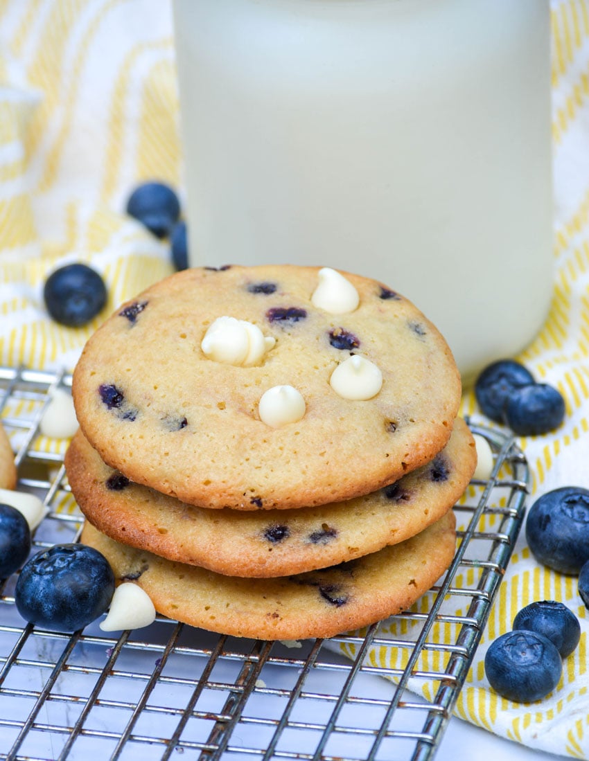 three blueberry cheesecake cookies stacked in front of a glass of milk
