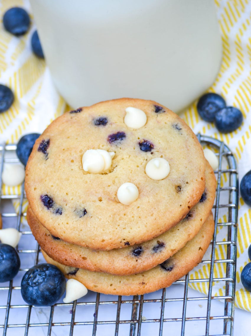 three blueberry cheesecake cookies stacked in front of a glass of milk