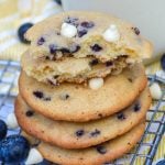 a stack of blueberry cheesecake cookies with white chocolate chips in front of a glass of milk