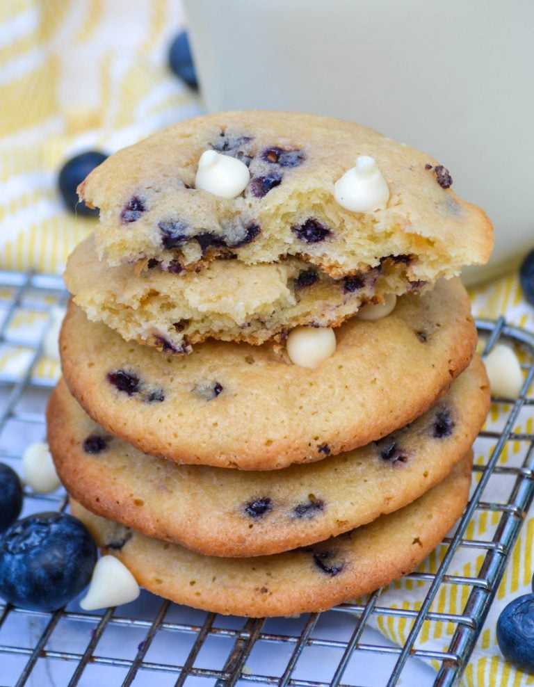 a stack of blueberry cheesecake cookies with white chocolate chips in front of a glass of milk