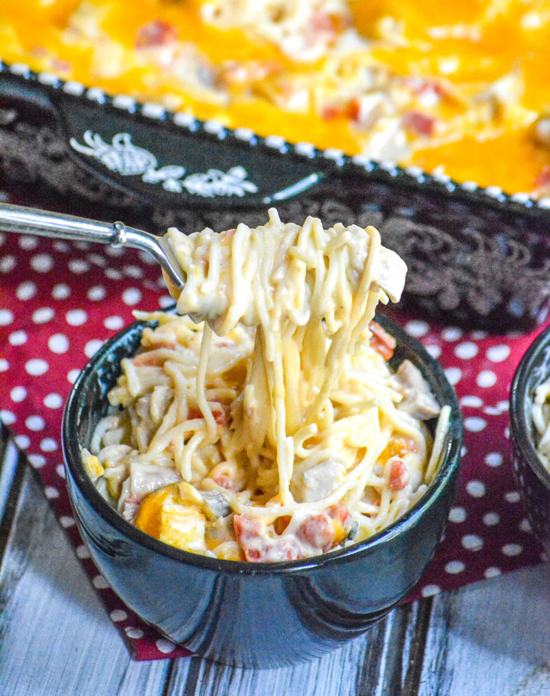 Cheesy Mexican Chicken Pasta Bake noodles wrapped around afork with chunks of chicken being held above a black bowl