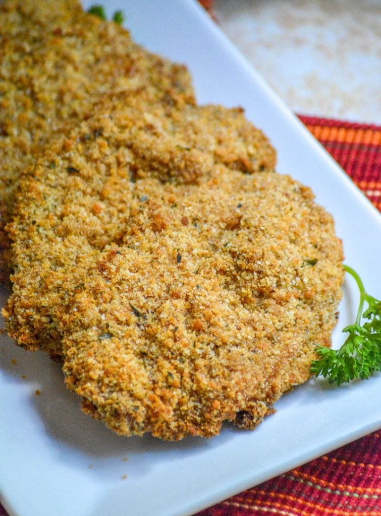 Crispy, Baked Italian Ranch Pork Chops on a white serving platter with a sprig of fresh parsley