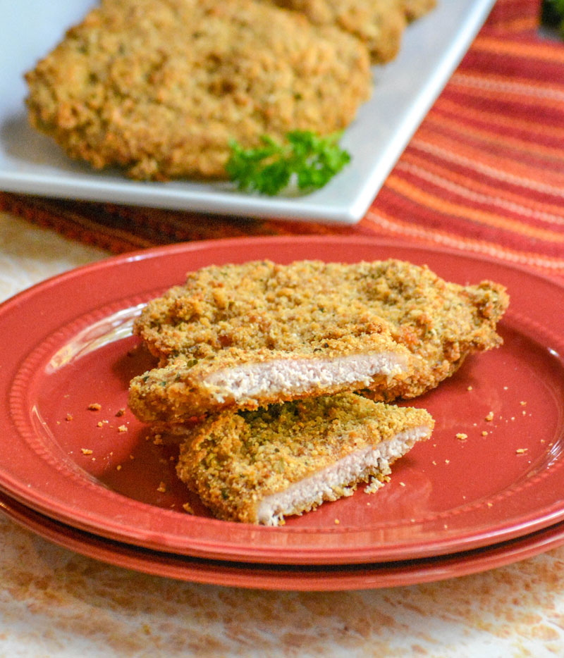 Crispy, Baked Italian Ranch Pork Chops sliced in half on a stack of red plates