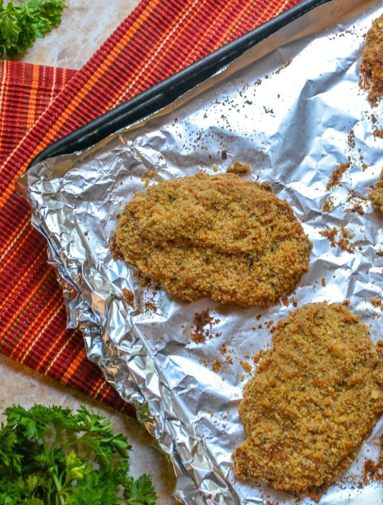 Crispy, Baked Italian Ranch Pork Chops on a foil lined baking sheet on top of a red napkin with fresh parsley