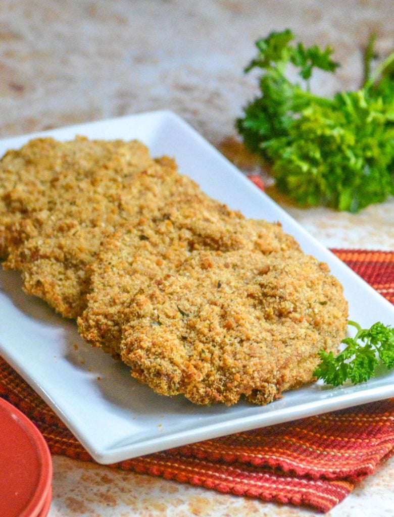 Crispy, Baked Italian Ranch Pork Chops on a white rectangular platter with a sprig of fresh parsley