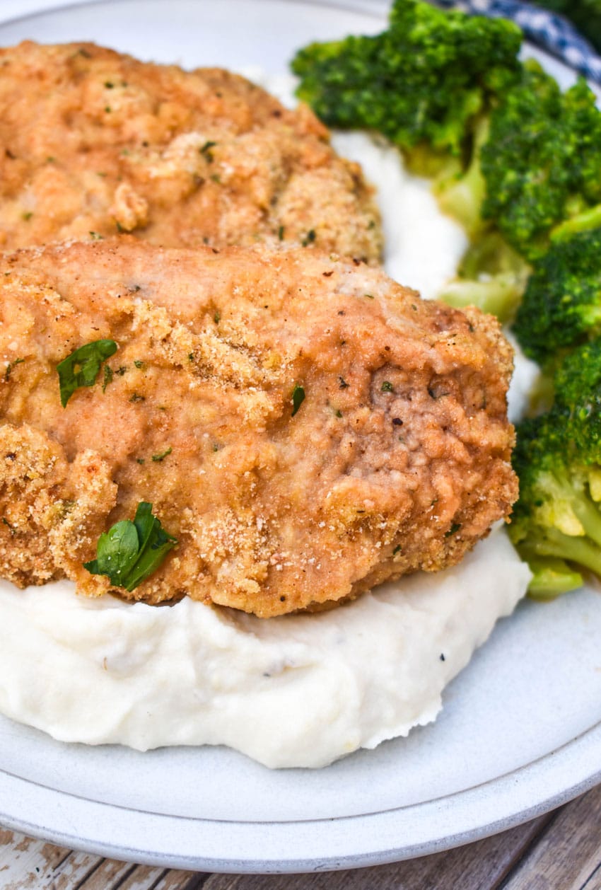 breaded pork chops with ranch dressing over mashed potatoes on a white plate with steamed broccoli on the side
