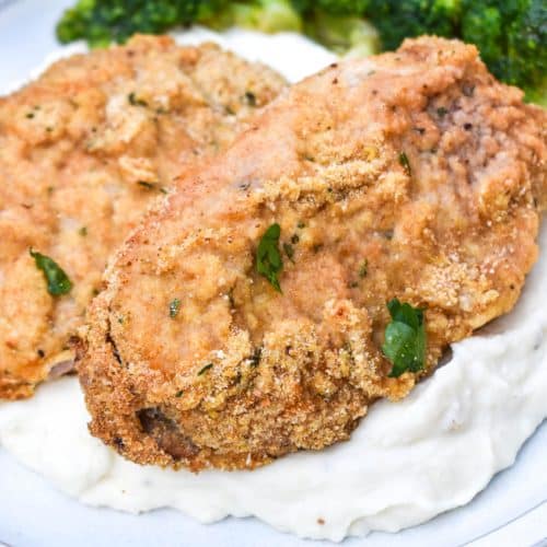 breaded pork chops with ranch dressing over mashed potatoes on a white plate with steamed broccoli on the side