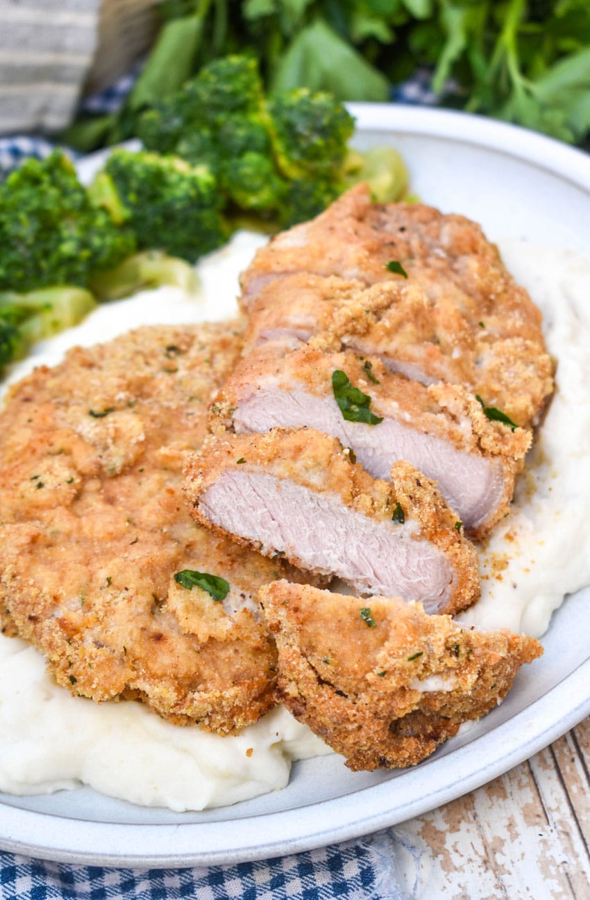 breaded pork chops with ranch dressing over mashed potatoes on a white plate with steamed broccoli on the side